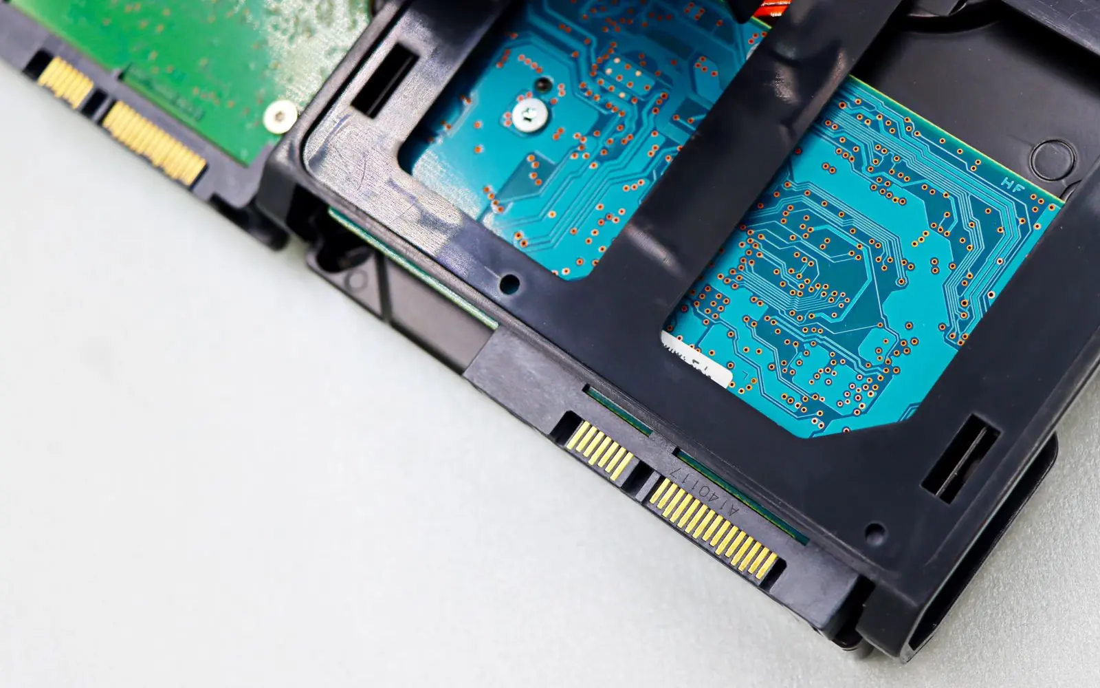Disque dur ouvert, circuit imprimé apparent, posé sur un fond clair