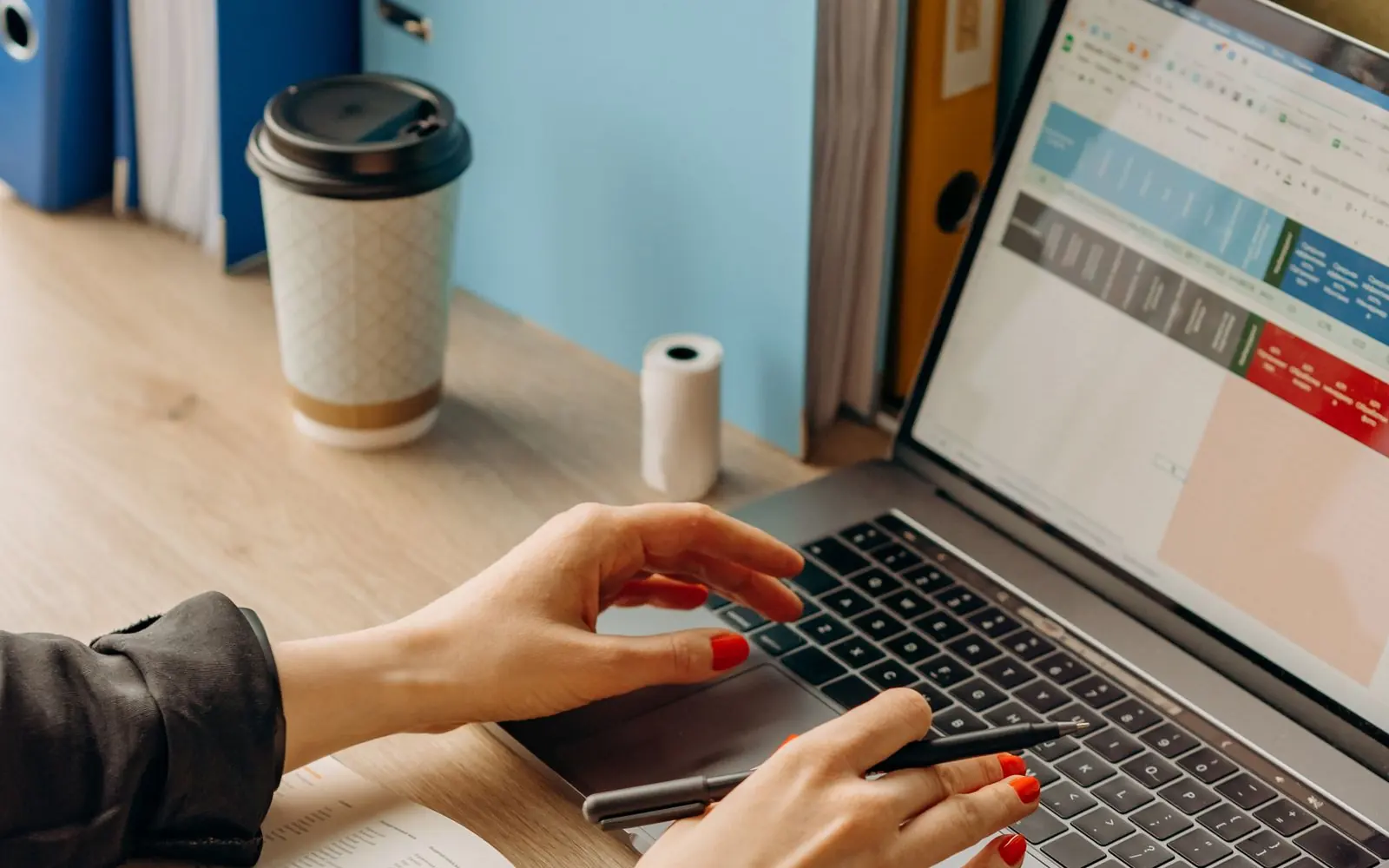 Mains sur le clavier d’un portable, classeurs de dossiers à côté